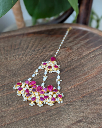 Gold-plated Indian choker necklace with pink gemstone stones and white pearl beads, displayed on a dark wooden surface.