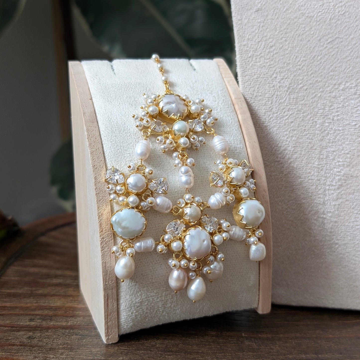 A gold and pearl bridal jewelry set featuring a matching headpiece and earrings, displayed on a cream-colored velvet jewelry stand.