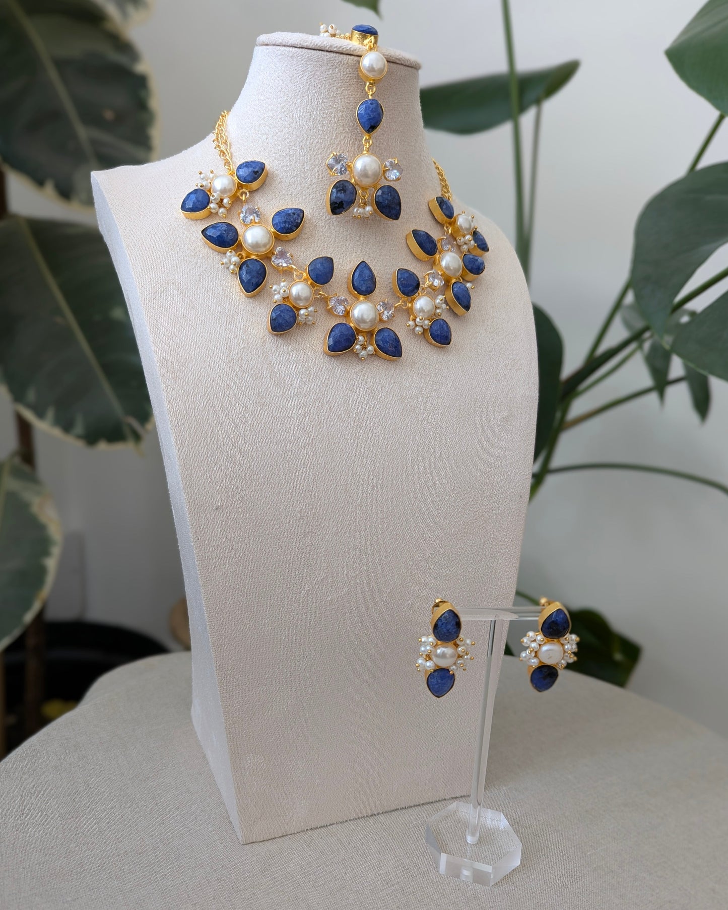 Jewelry set with blue and gold elements on a white stand against a neutral background