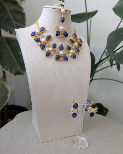 Jewelry set with blue and gold elements on a white stand against a neutral background