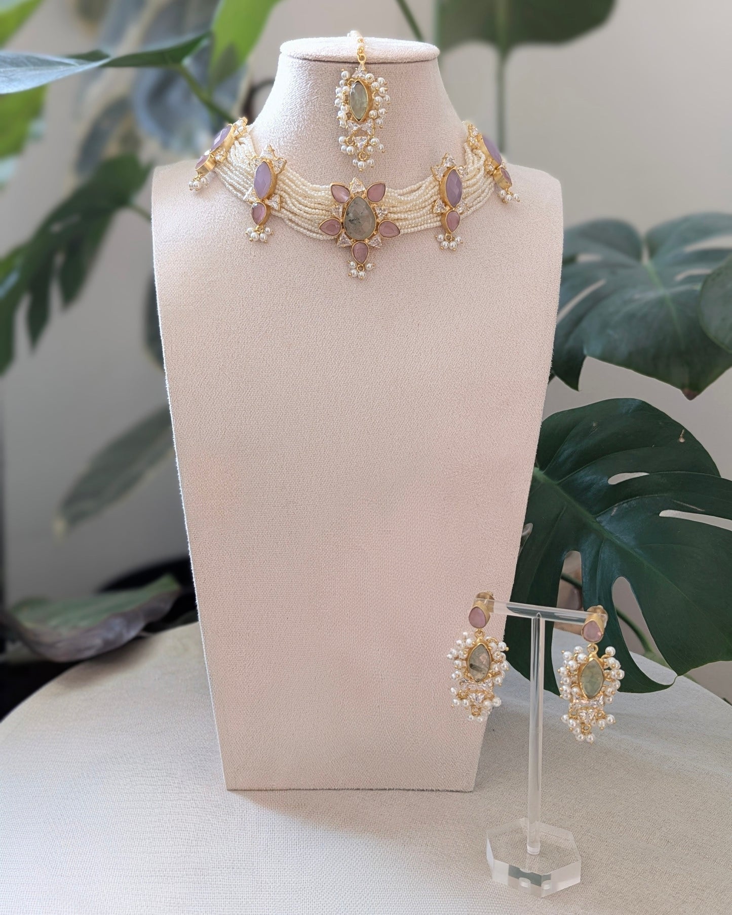 Jewelry set including necklace and earrings on a white stand with green leaves in the background
