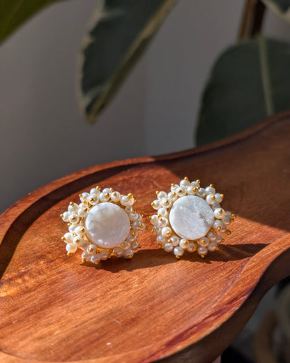 Pair of earrings with white stones and gold accents on a wooden surface.