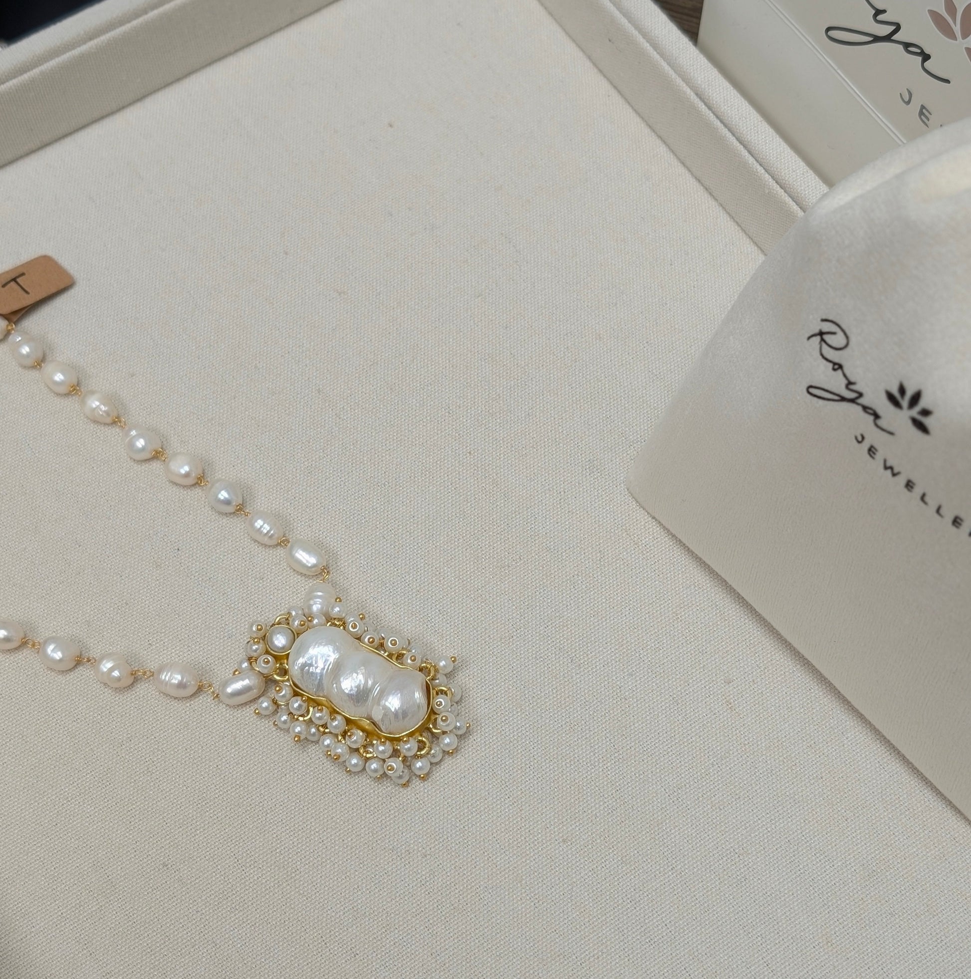 Pearl necklace on a branded jewelry box with 'Roya' bags